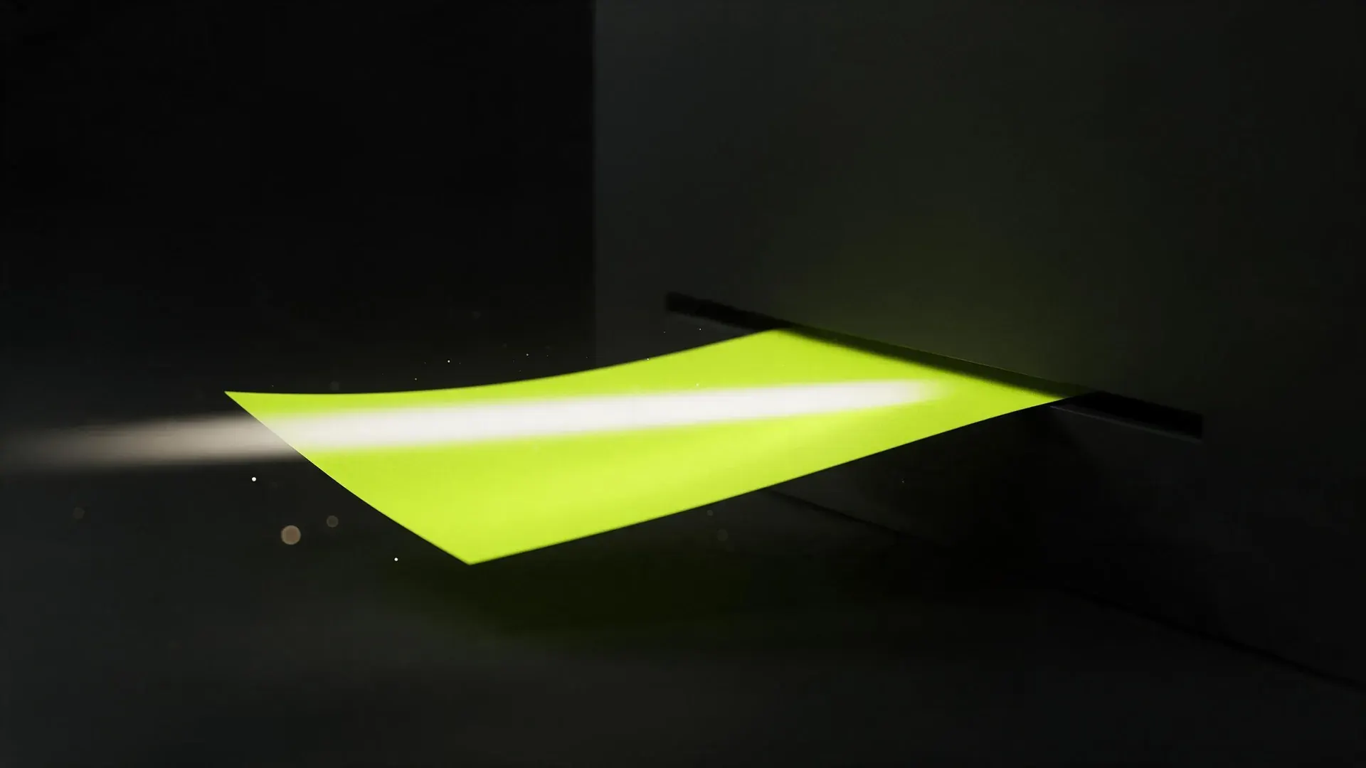A lime sheet feeding through a narrow slot in a dark panel, a bar of light sweeping across it.